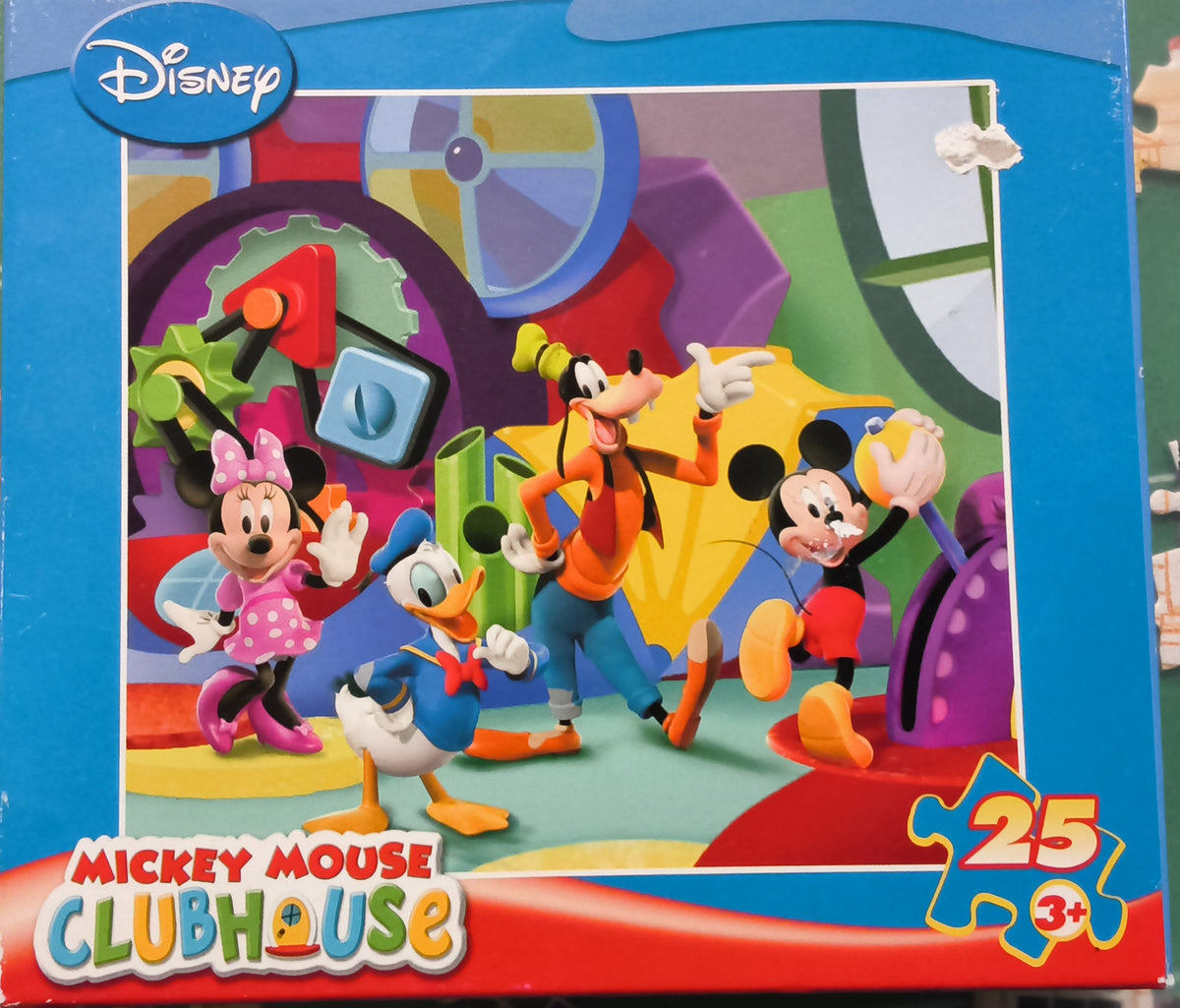 A Disney Clubhouse Mickey Mouse 25-piece jigsaw puzzle box on a green puzzle mat with loose puzzle pieces scattered around.
