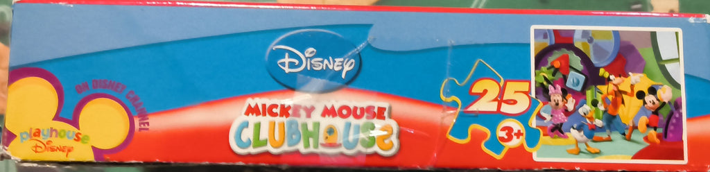 A boxed Disney Mickey Mouse Clueless jigsaw puzzle package standing upright on a green puzzle mat with scattered puzzle pieces around it.