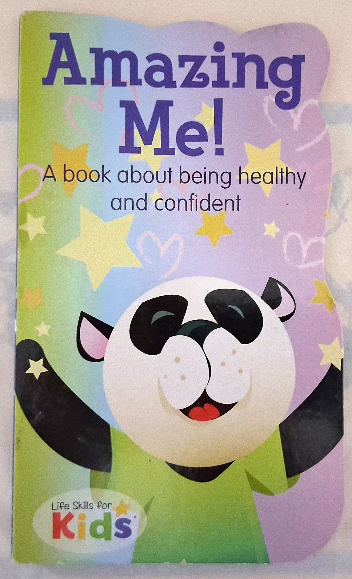 Front cover of the children's book 'Amazing Me! A book about being healthy and confident' by Life Skills for Kids, featuring a smiling panda illustration on a pastel rainbow background.
