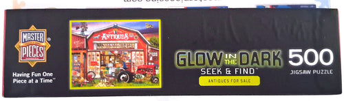 A 500-piece jigsaw puzzle box by Master Pieces featuring a red barn and tractor illustration, with text reading 'Glow in the Dark Seek & Find' and 'Antiques for Sale.'.