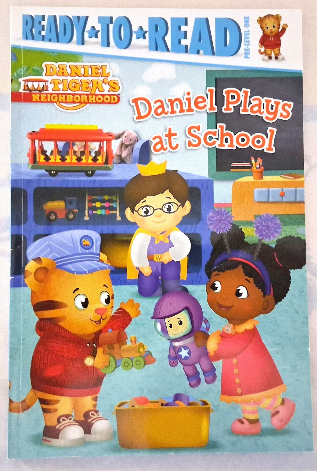 Daniel Tiger's Neighborhood 'Daniel Plays at School' ready-to-read children's book cover, featuring colorful cartoon illustrations of Daniel Tiger, Daniel's tiger family, and other neighborhood characters in a school setting.