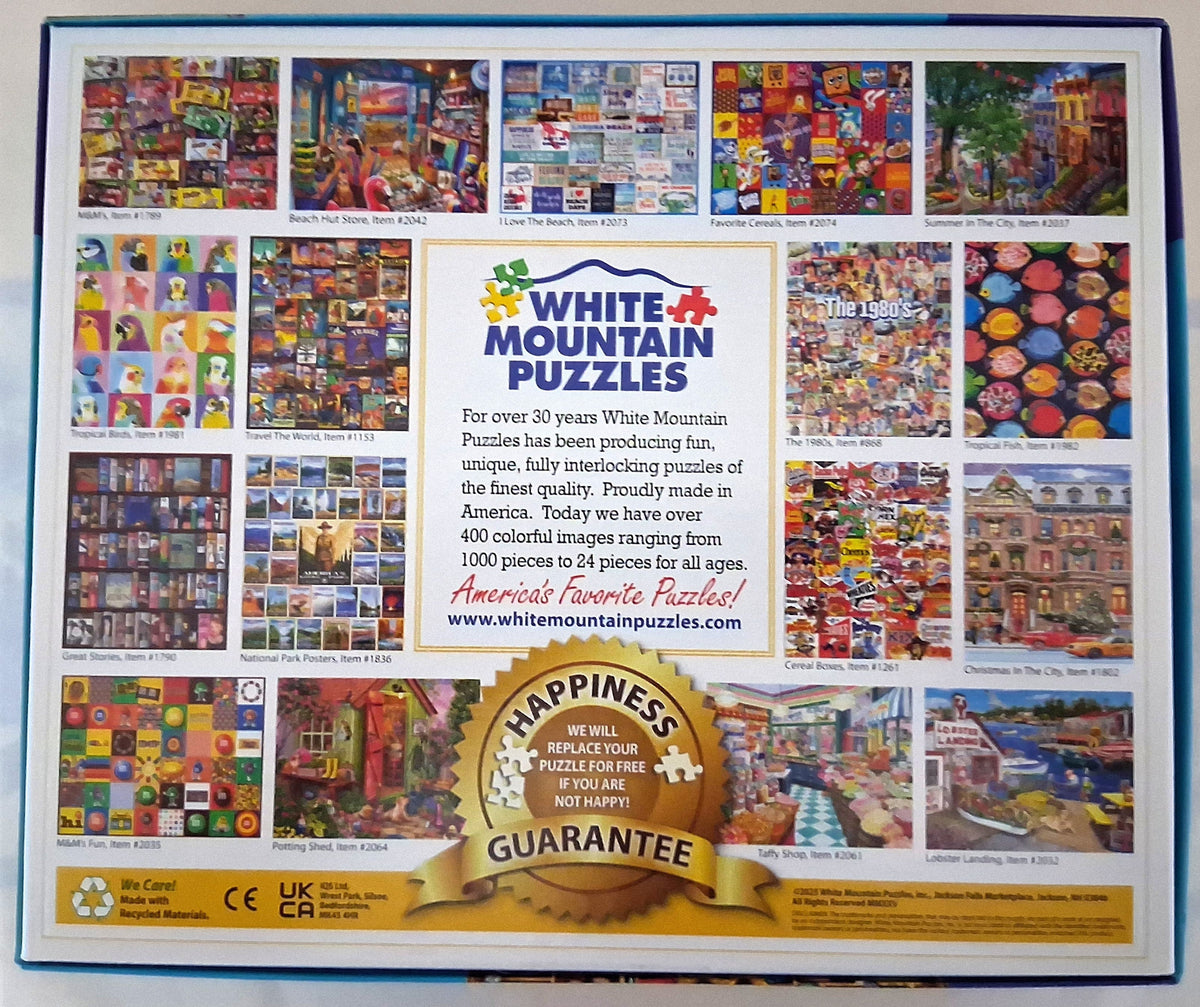 The back cover of a White Mountain Puzzles jigsaw puzzle box, featuring a grid of colorful sample puzzle images, product description text, and a gold 'Happiness Guarantee' seal.