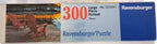 Ravensburger 300-piece jigsaw puzzle box featuring a lakeside scene with two red Adirondack chairs on a wooden deck, alongside text reading '300 Large Piece Format Pieces' and the Ravensburger brand.

