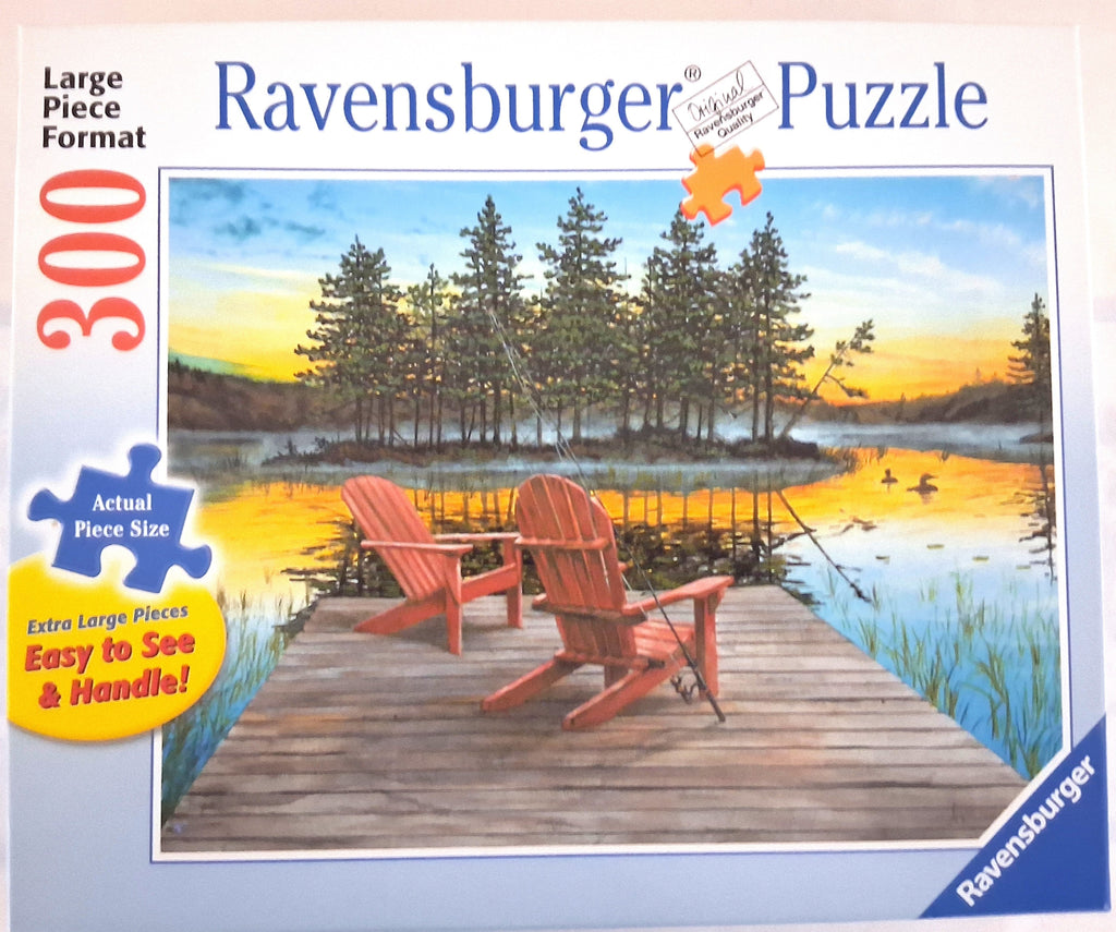Ravensburger 300-piece jigsaw puzzle box featuring a scenic lake sunset with two red Adirondack chairs on a wooden dock, trees, and ducks. The box includes product text and graphics on a white background.