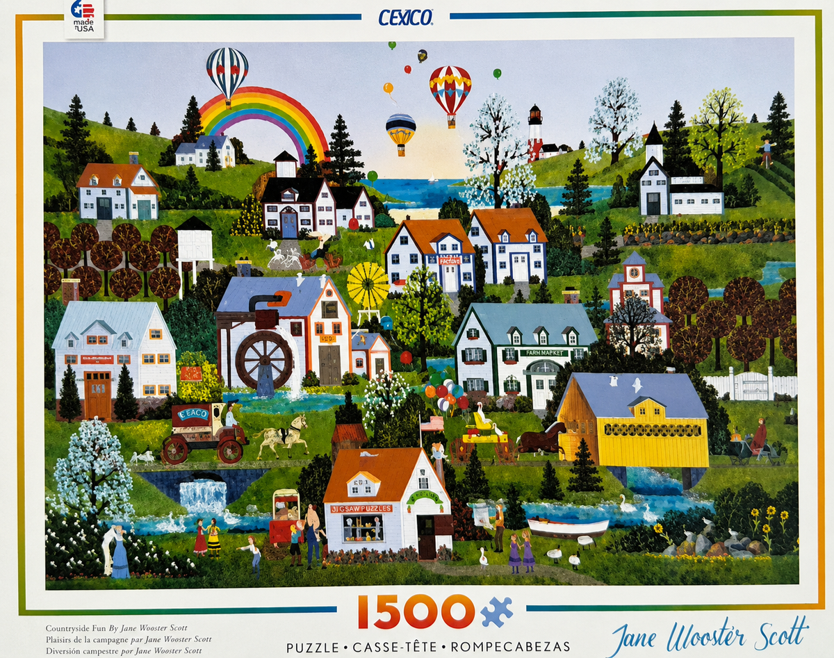Front cover of a CEACO 1500-piece jigsaw puzzle featuring a colorful folk-art style village scene with houses, hot air balloons, trees, and a rainbow, designed by Jane Wooster Scott.